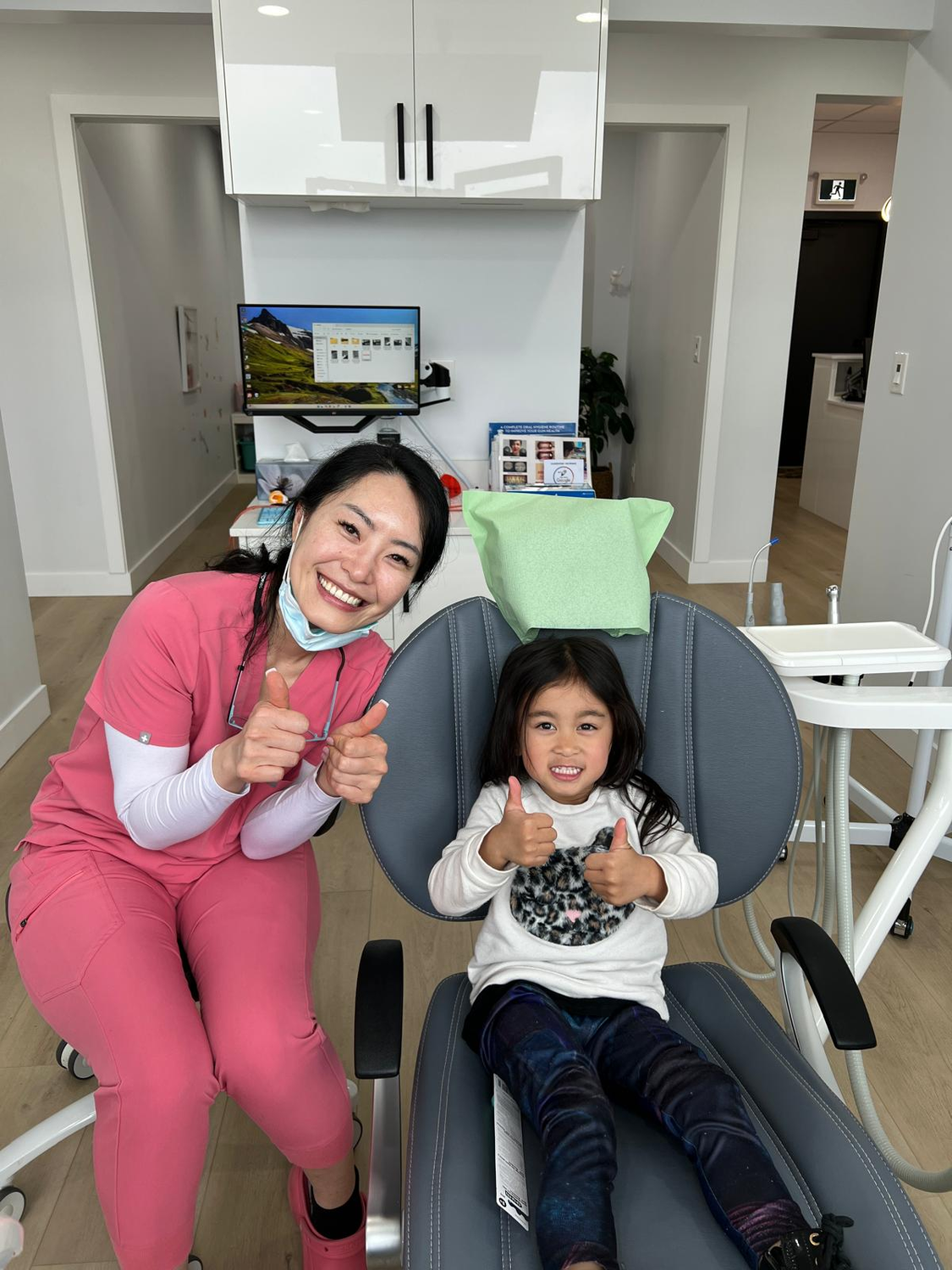 A smiling Aviator dental hygienist and a young child giving a thumbs up together after the child's first cleaning