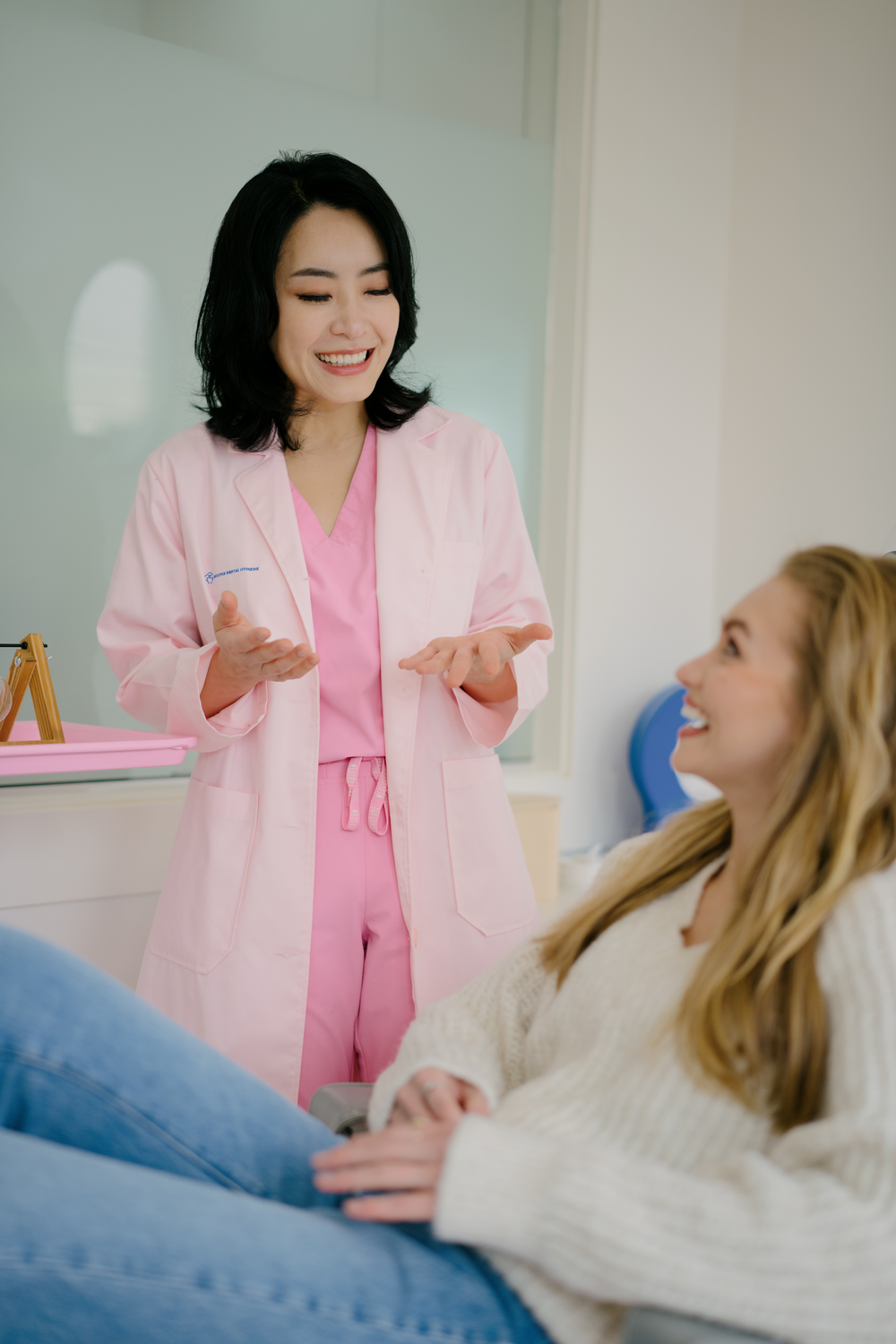 A friendly dental hygienist in pink chatting warmly with a relaxed, smiling patient at Aviator