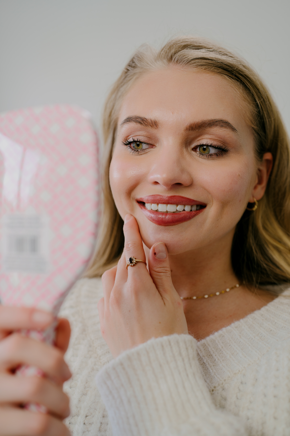 A patient checking her bright, natural smile in a hand mirror after a cleaning at Aviator
